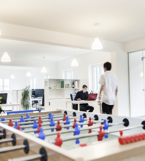 Ein Mitarbeiter am Laptop und ein zweiter Mitarbeiter, der durch den Raum geht.